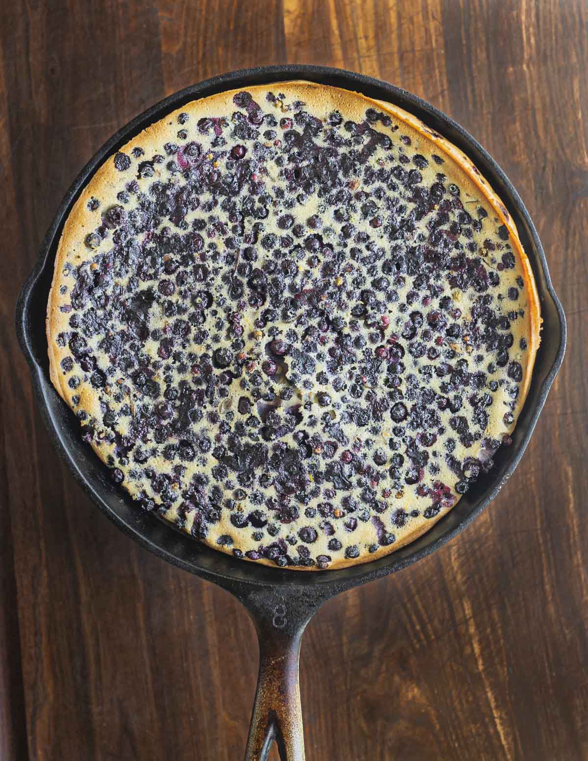 A cooked and perfectly browned blueberry clafoutis in a cast iron pan. 