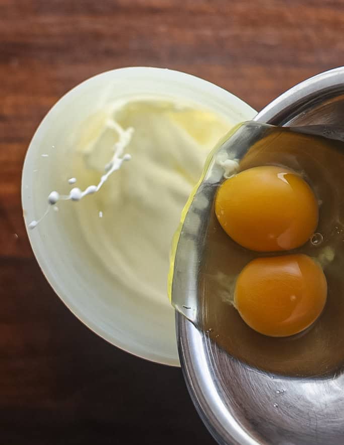 Adding whole eggs to a blueberry clafoutis batter. 
