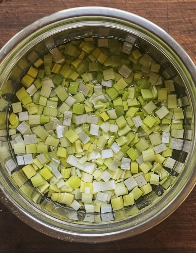 Finely diced leeks being washed in a bowl of water to remove any dirt. 