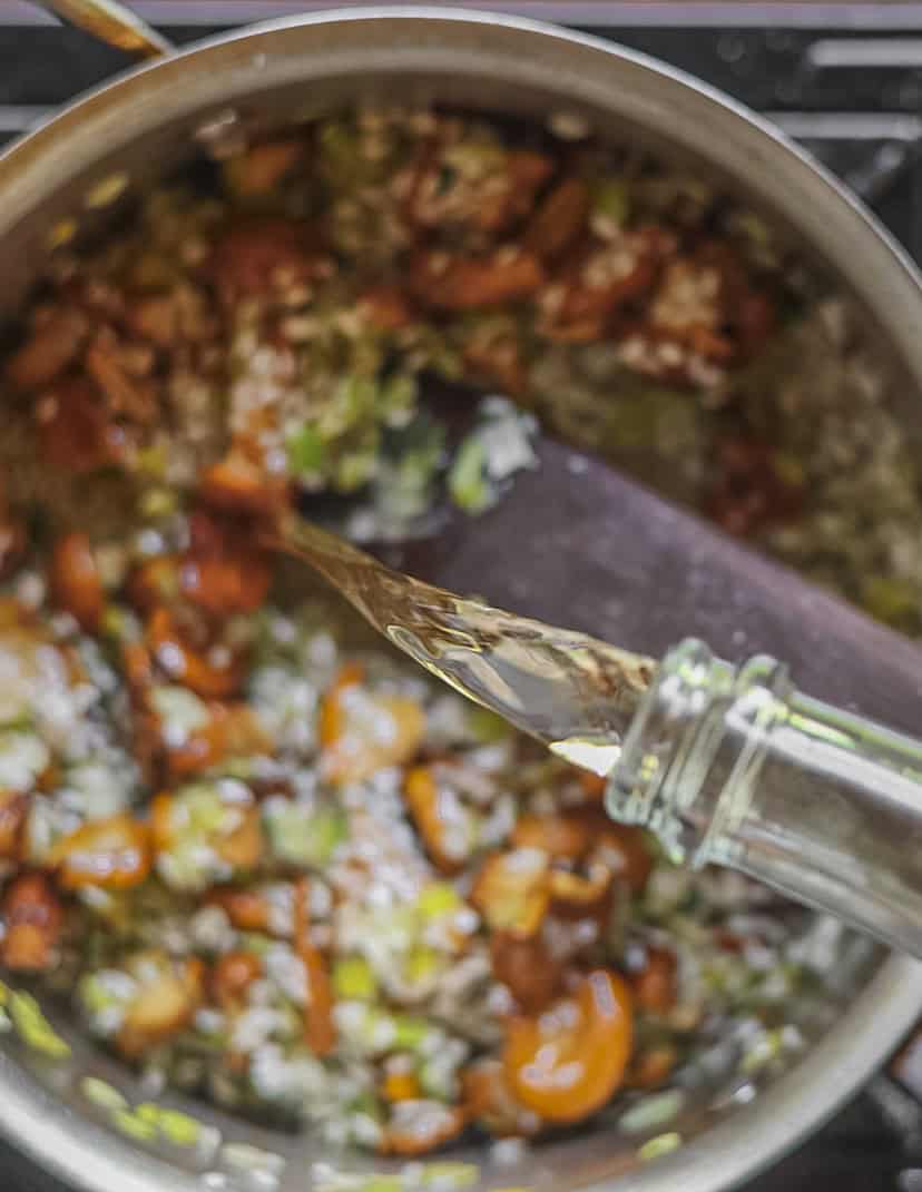 Pouring a splash of dry white wine into a pan of chanterelle mushroom risotto. 