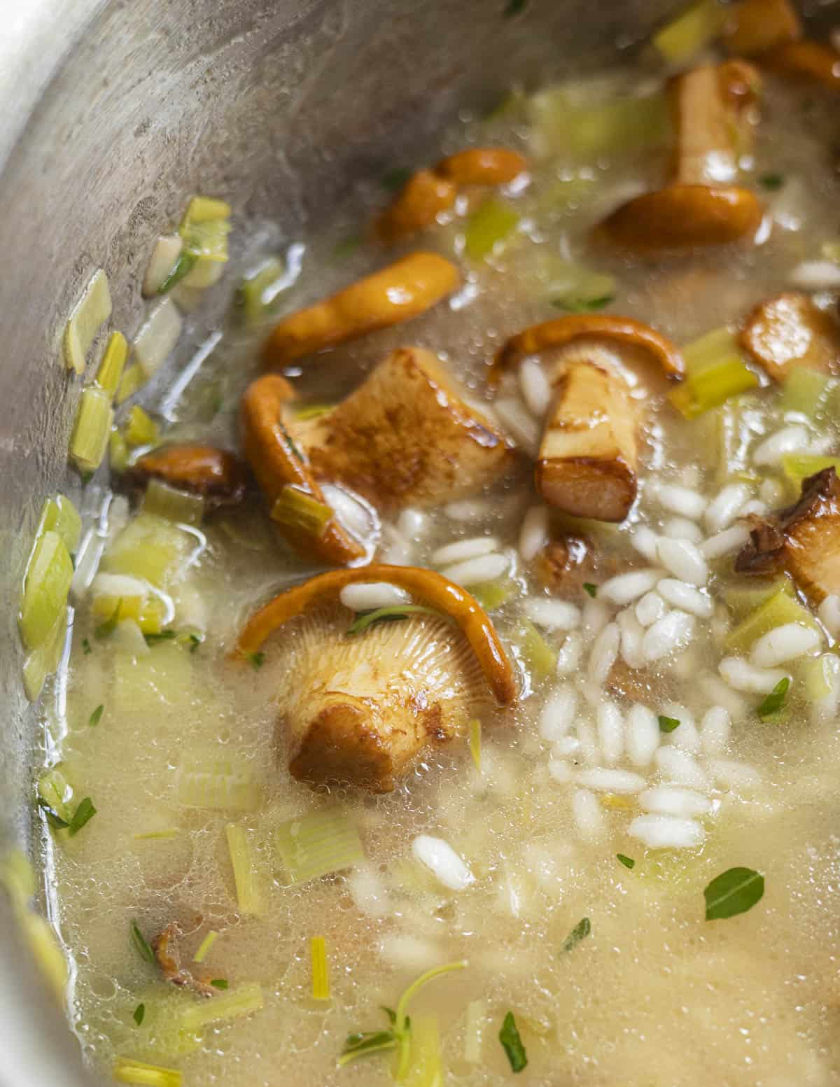 A close up image of chanterelle mushrooms in a pan simmering with risotto rice and leeks. 