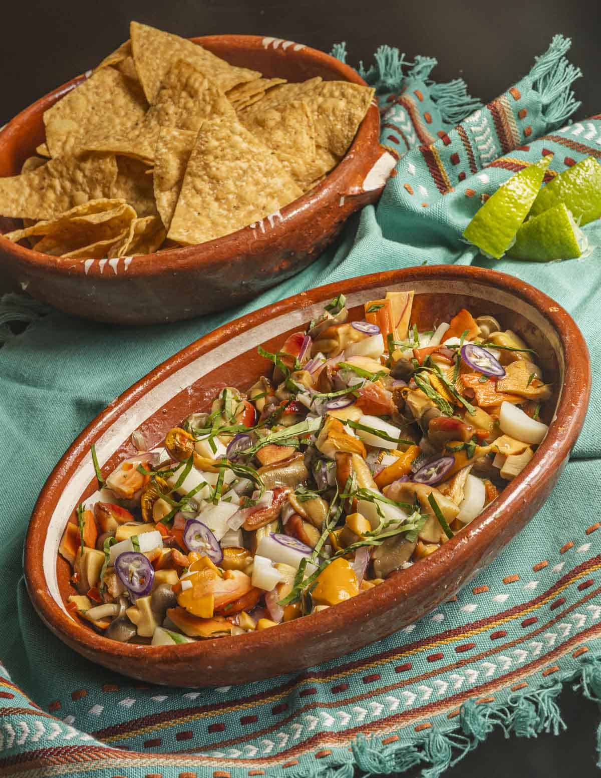 A dish of wild mushroom ceviche garnished with herbs and lime served with tortilla chips. 