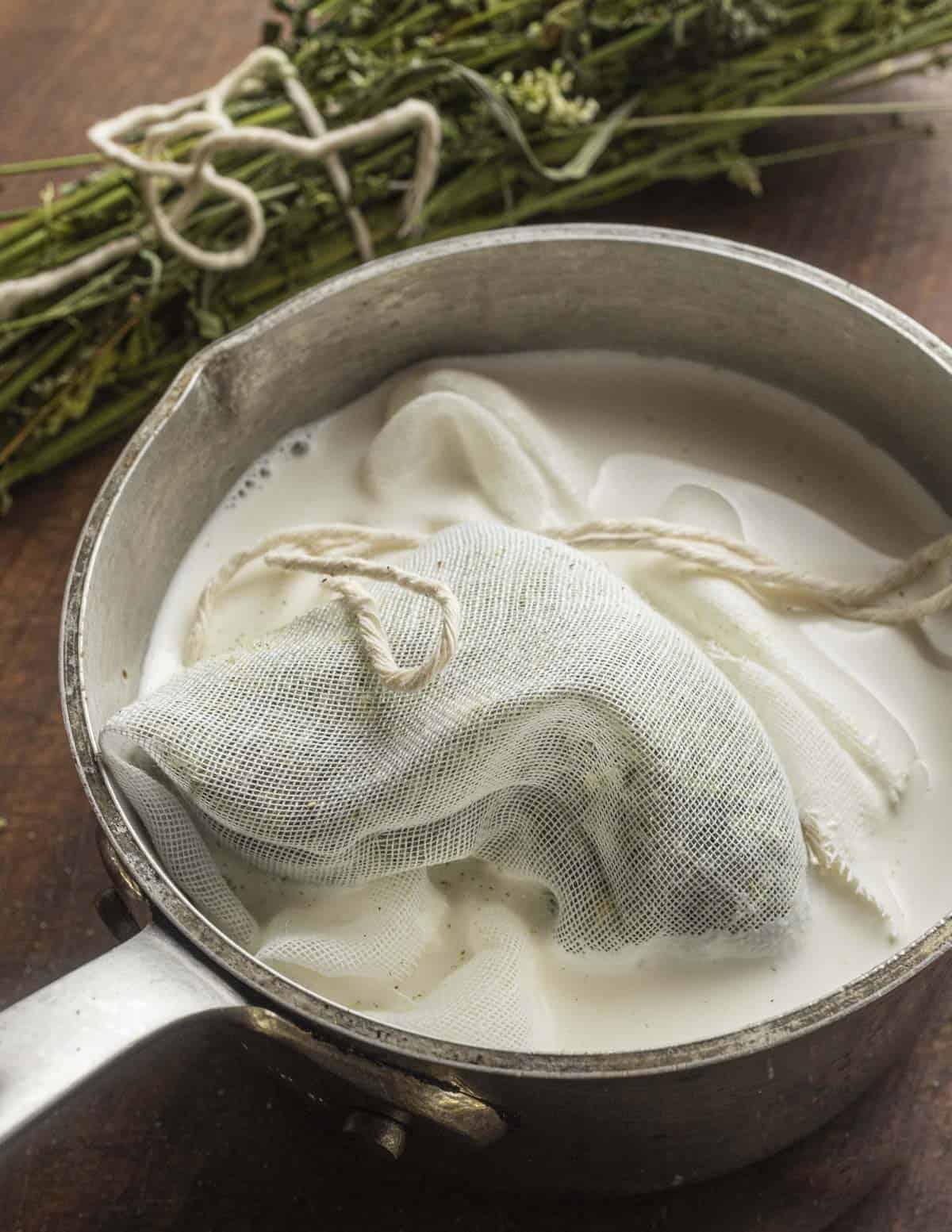 A sachet of dried sweet clover in a pan of heavy cream ready to cook with dried sweet clover in the background. 