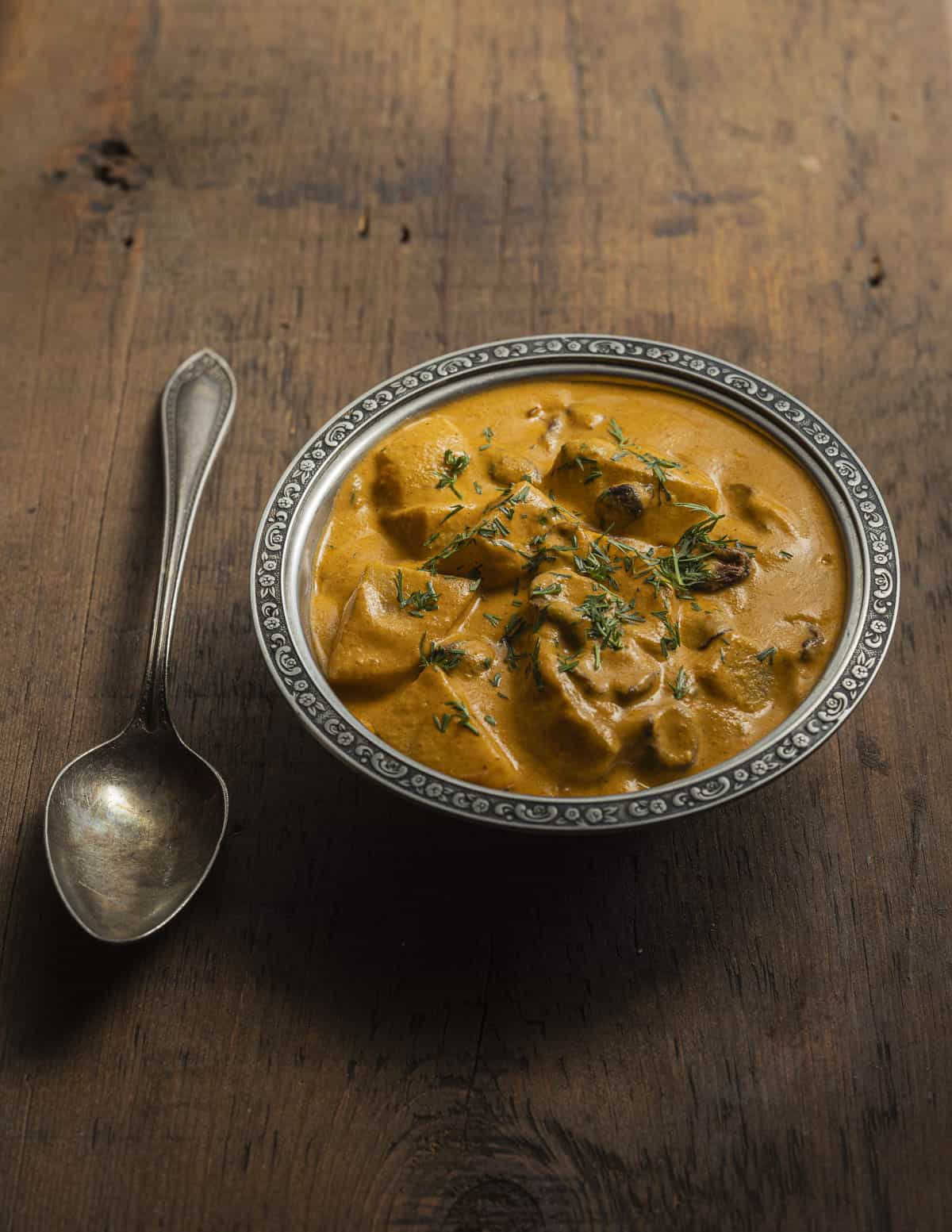 A bowl of potato and puffball curry makhani garnished with chopped wild caraway leaves. 