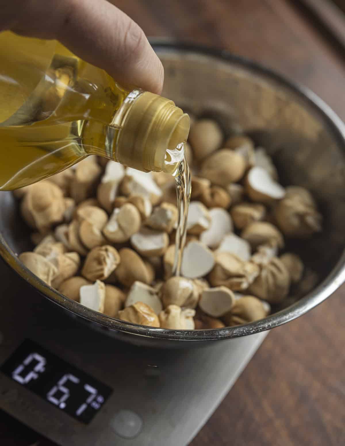 Pouring cooking oil into a bowl of small puffball mushrooms seasoned with salt. 