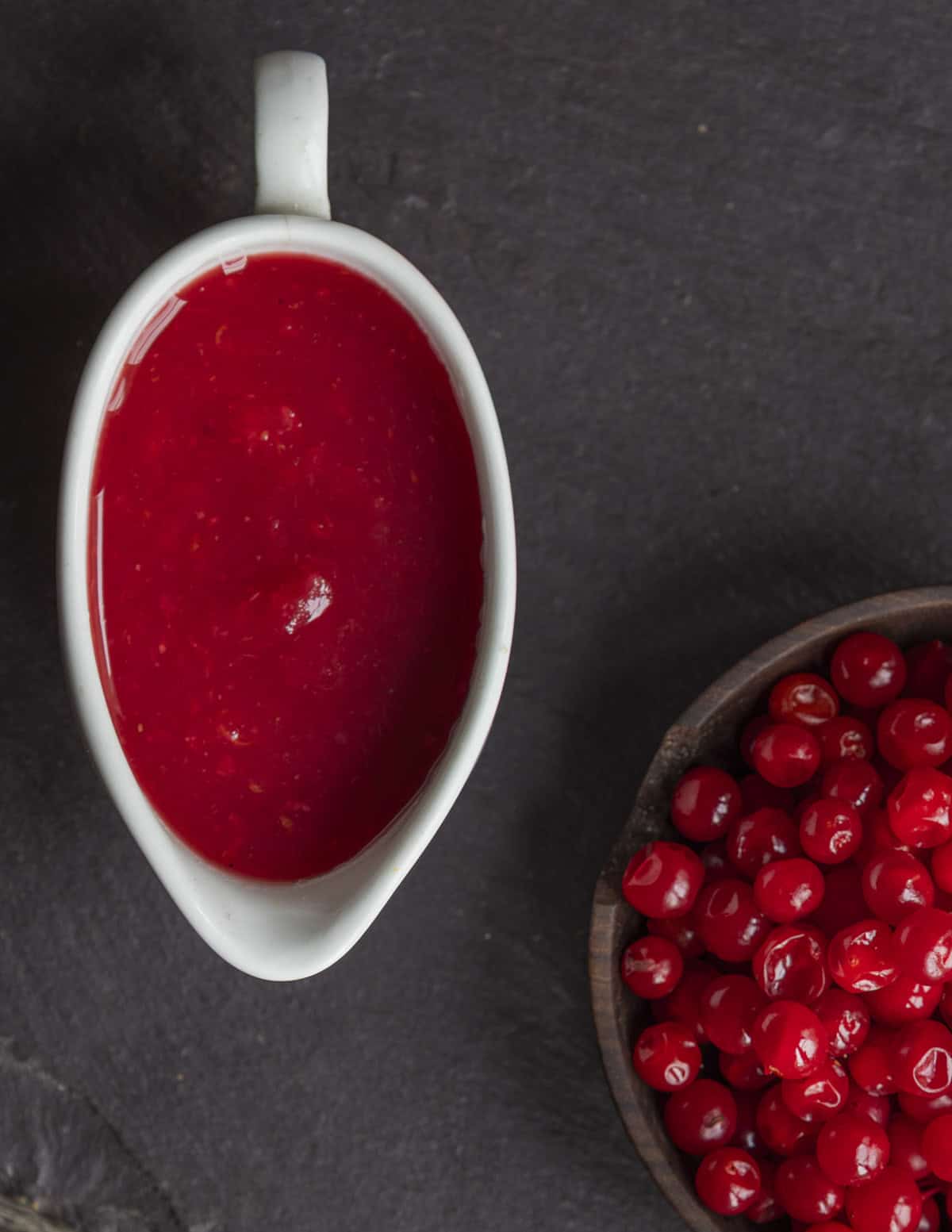 A small boat of high bush cranberry sauce next to a bowl of ripe fruit. 