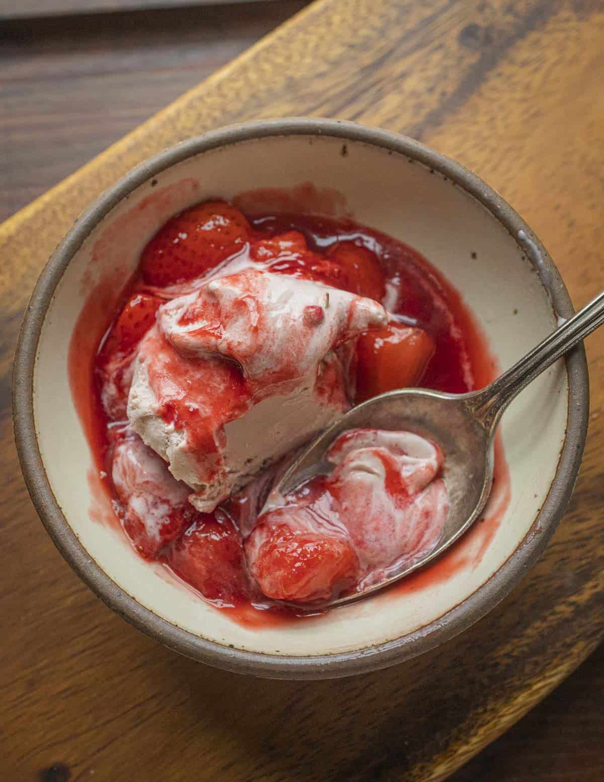 A bowl of vanilla ice cream with highbush cranberry puree and strawberries. 