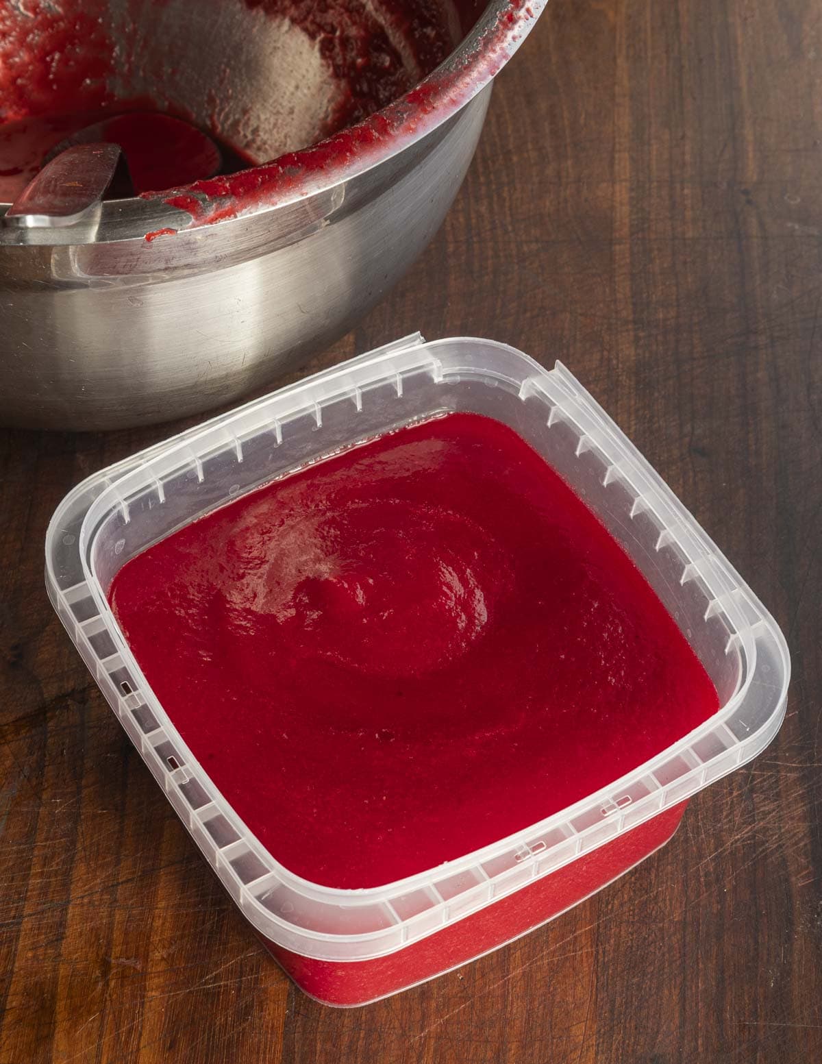 A container of finished highbush cranberry puree in a deli container next to a bowl of puree. 