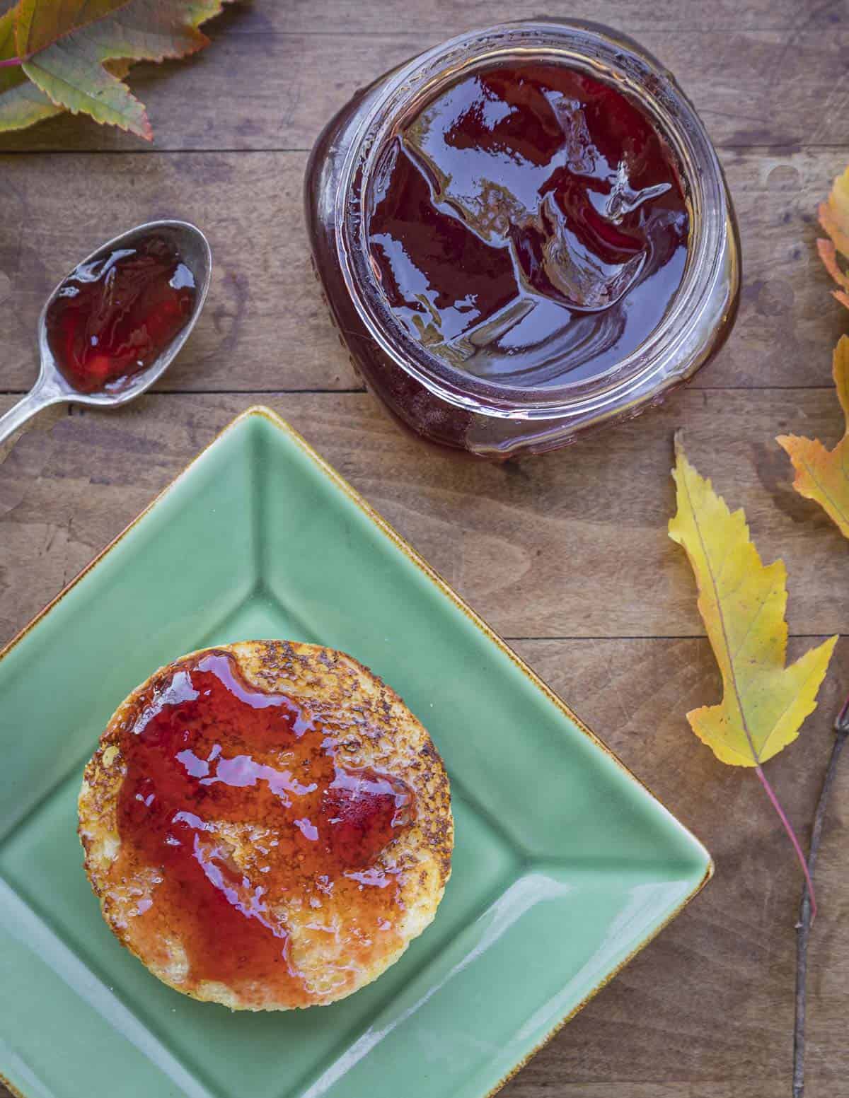 Highbush cranberry jelly on a piece of buttered bread next to a jar of jelly and highbush cranberry leaves. 