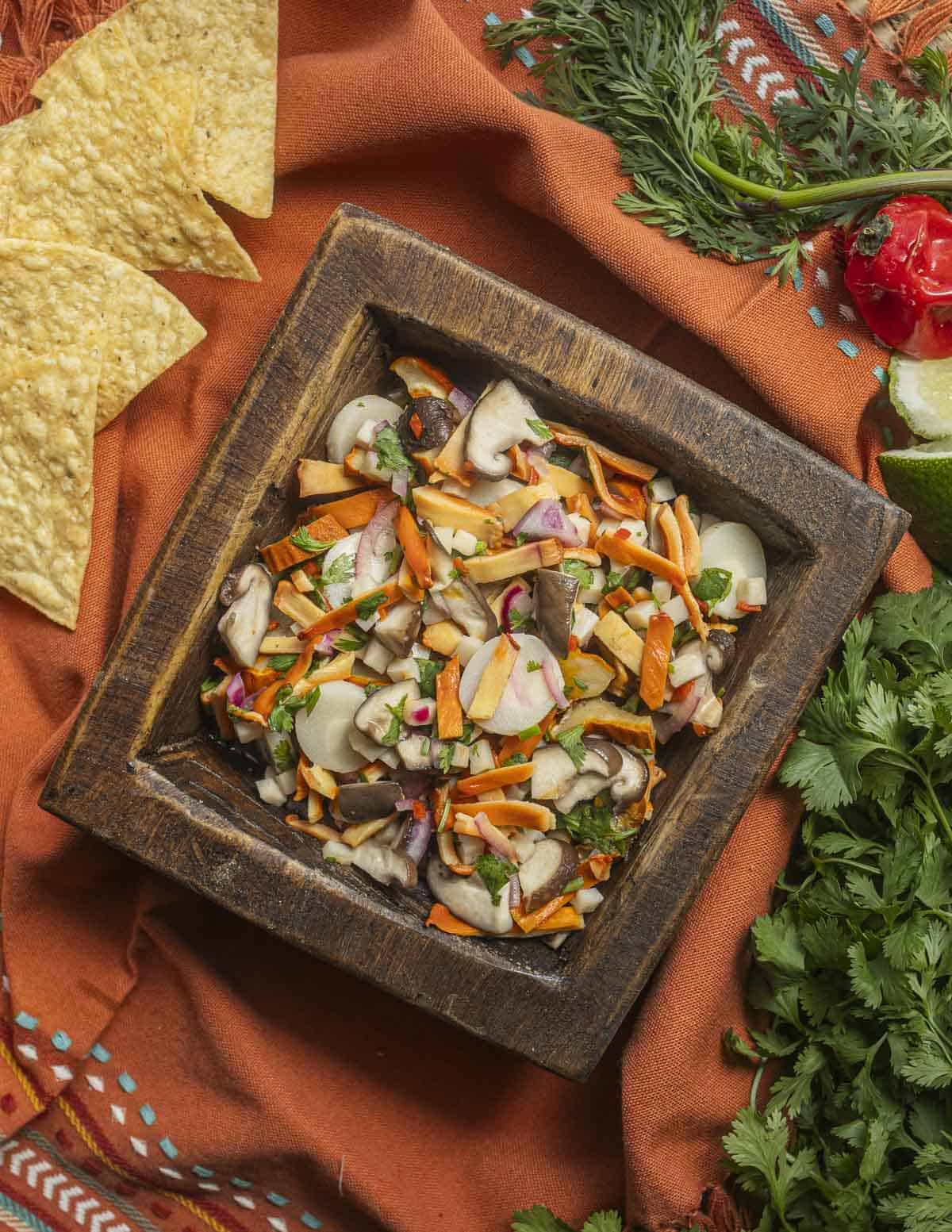 Mushroom Ceviche in a wooden dish surrounded by Hmong cilantro, a habanero pepper and tortilla chips.
