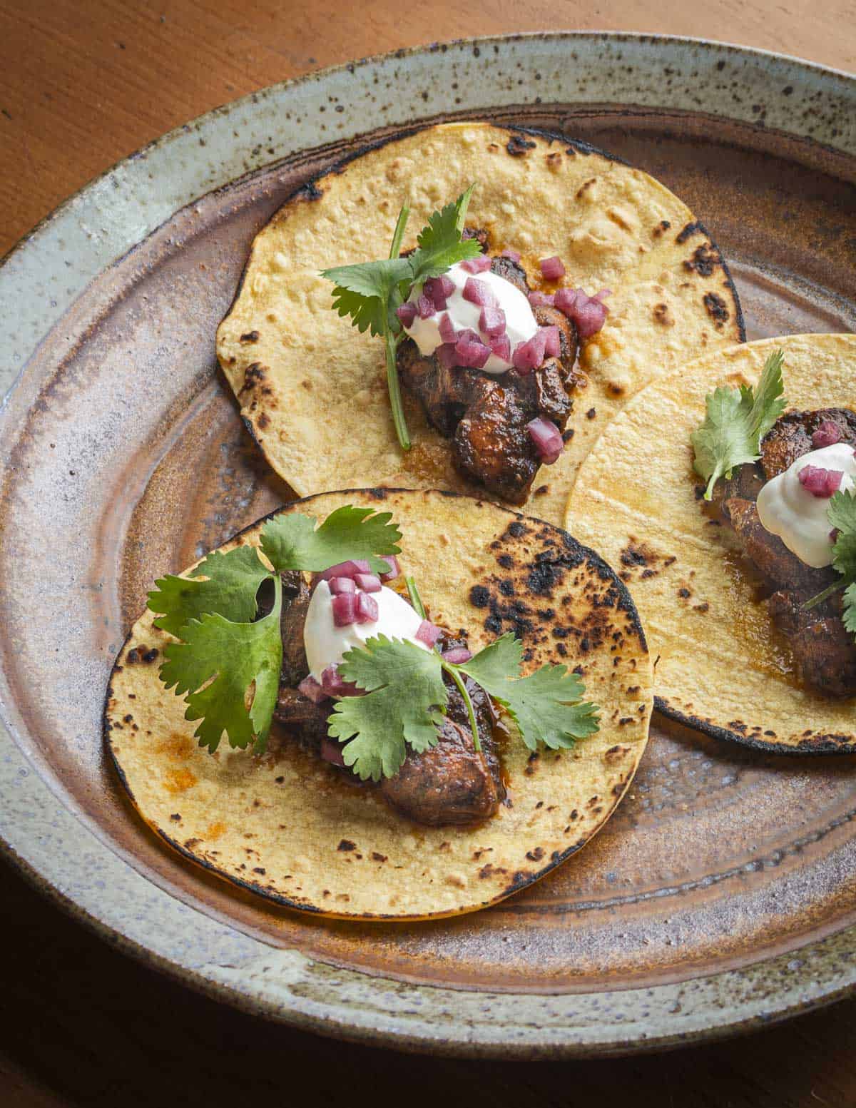 Three puffball mushroom tacos on charred corn tortillas garnished with cilantro, sour cream and pickled onions.