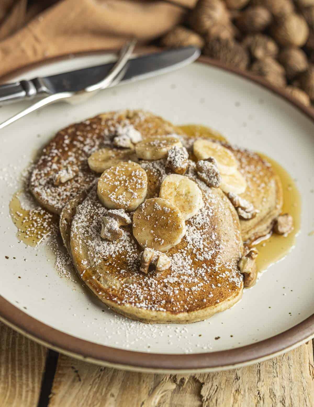 A finished plate of banana walnut pancakes garnished with fresh bananas and black walnuts and dusted with spicebush sugar. 