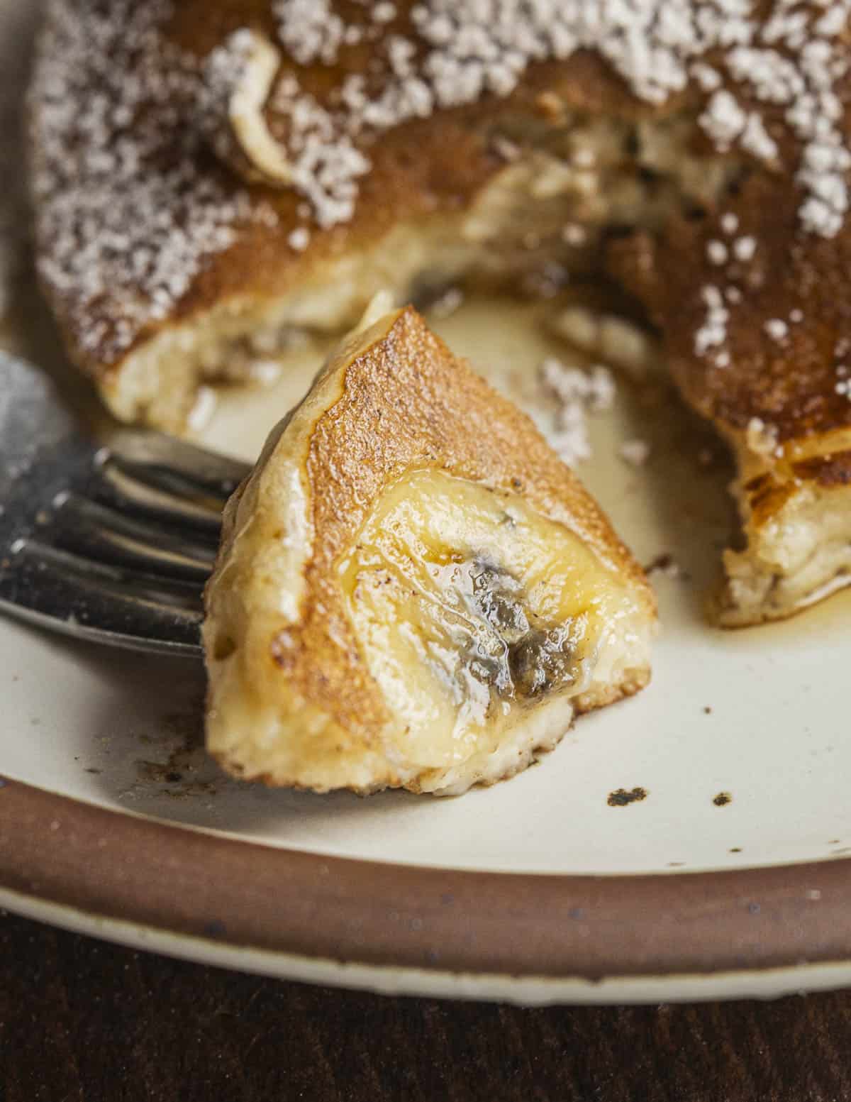 A close up image of a fork cutting into a pancake with bananas inside. 