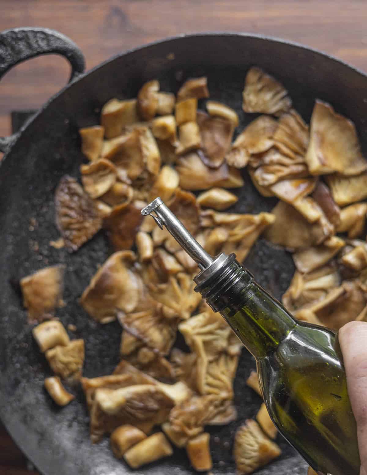Adding cooking oil to a pan of fried chicken mushrooms after the water's cooked off. 