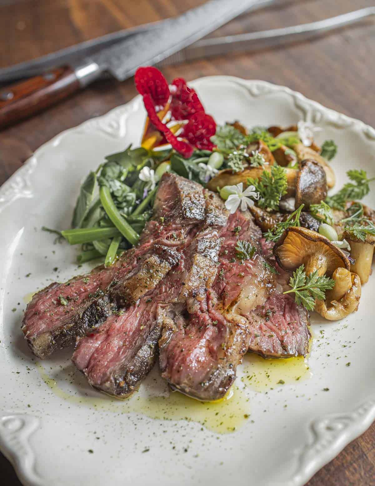 A bavette steak sliced and served with fried chicken mushrooms, herbs and cooked leafy greens.