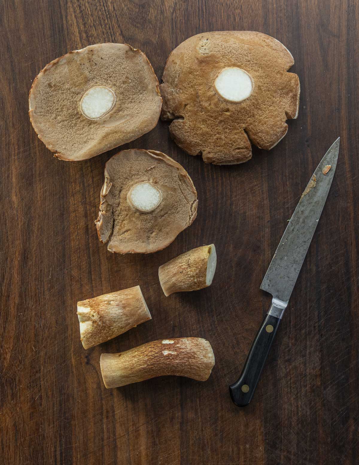 Cutting the stems from mature bolete mushrooms (Boletus subcaerulescens), showing bug free stems on a cutting board.
