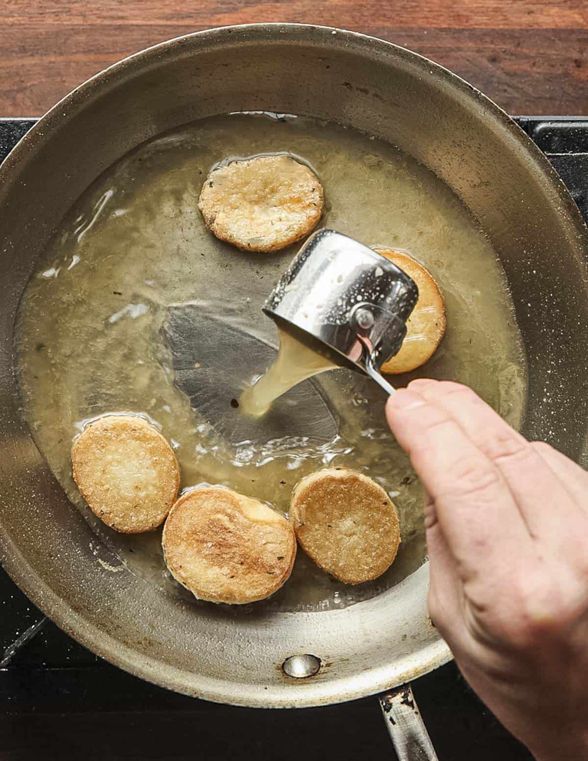 Adding chicken stock to a pan of mushroom scallops made from King oyster mushroom stems.