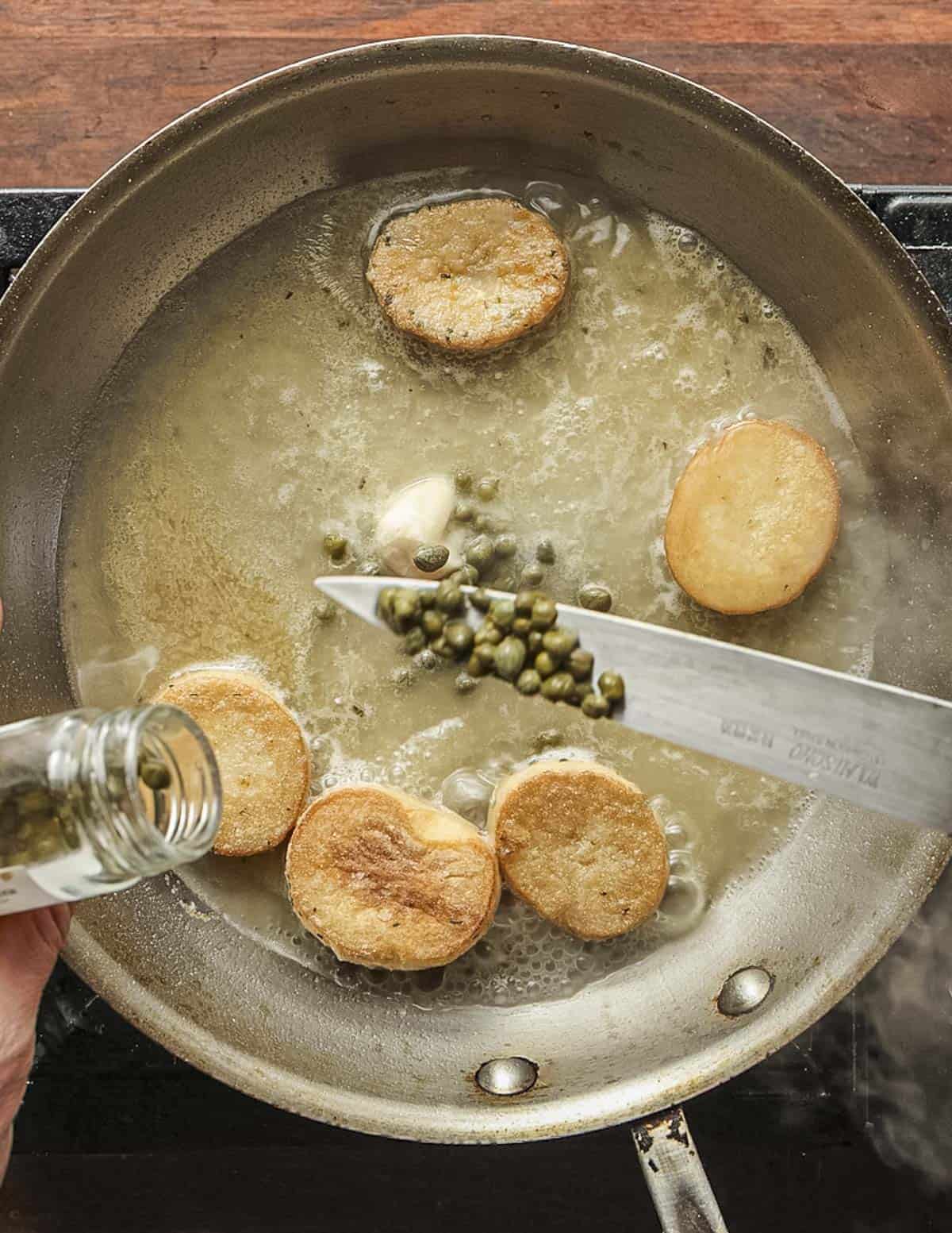 Adding capers and roux to a pan of King oyster mushroom scallops.