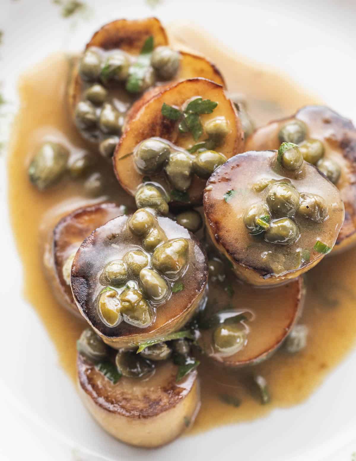 A close-up image of sautéed Porcini mushroom scallops made from bowl, mushroom stems in a lemon wine and caper sauce, garnished with chopped parsley