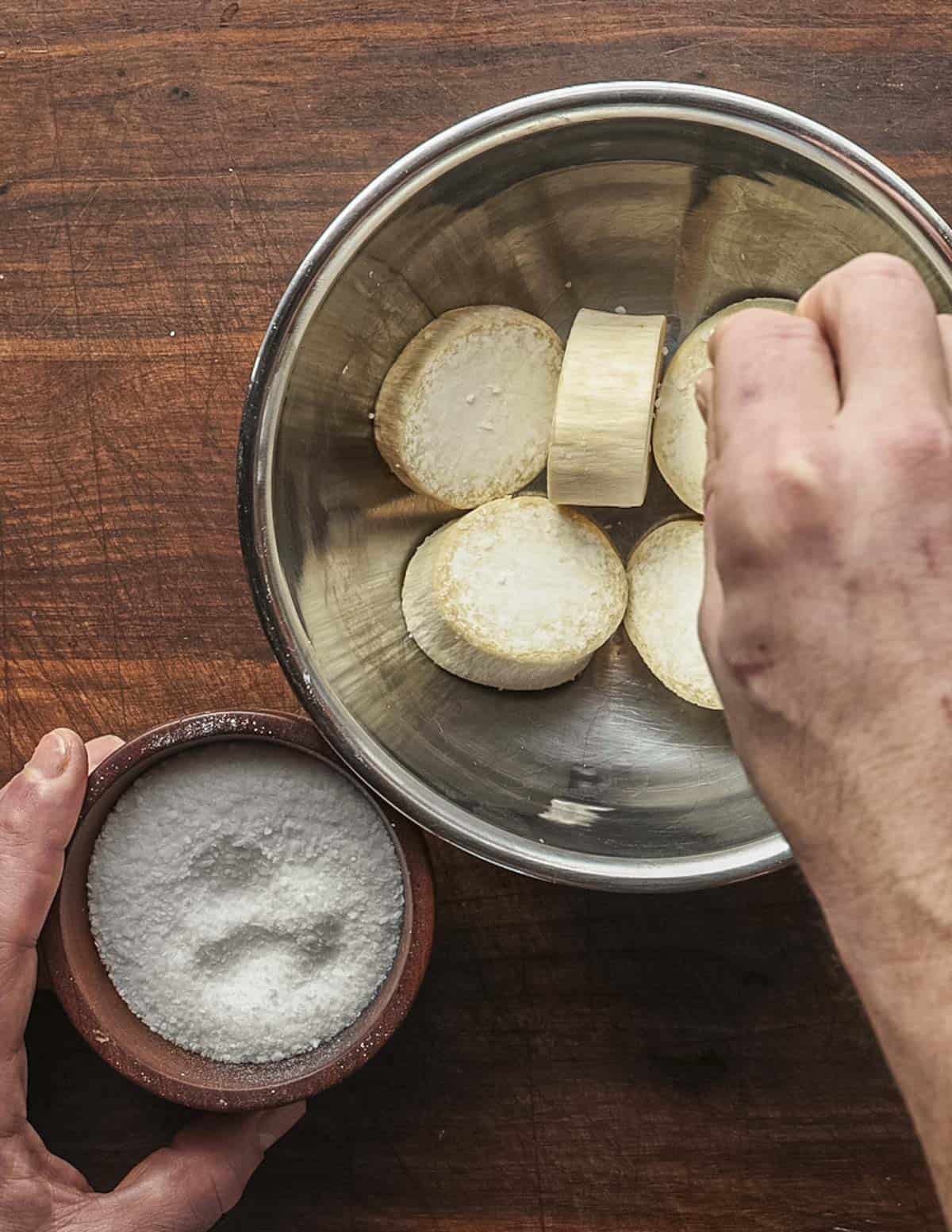 Tossing thick, sliced king oyster mushroom scallops in a bowl with salt.
