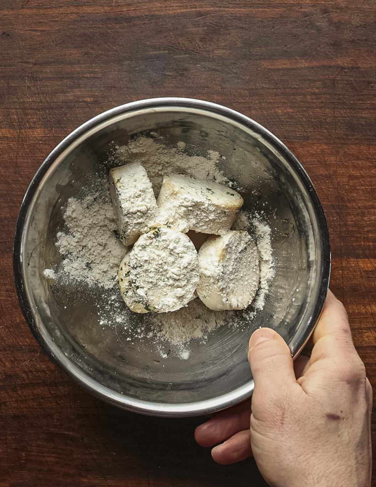 Tossing salted King oyster mushroom slices in all purpose flour in a metal mixing bowl.