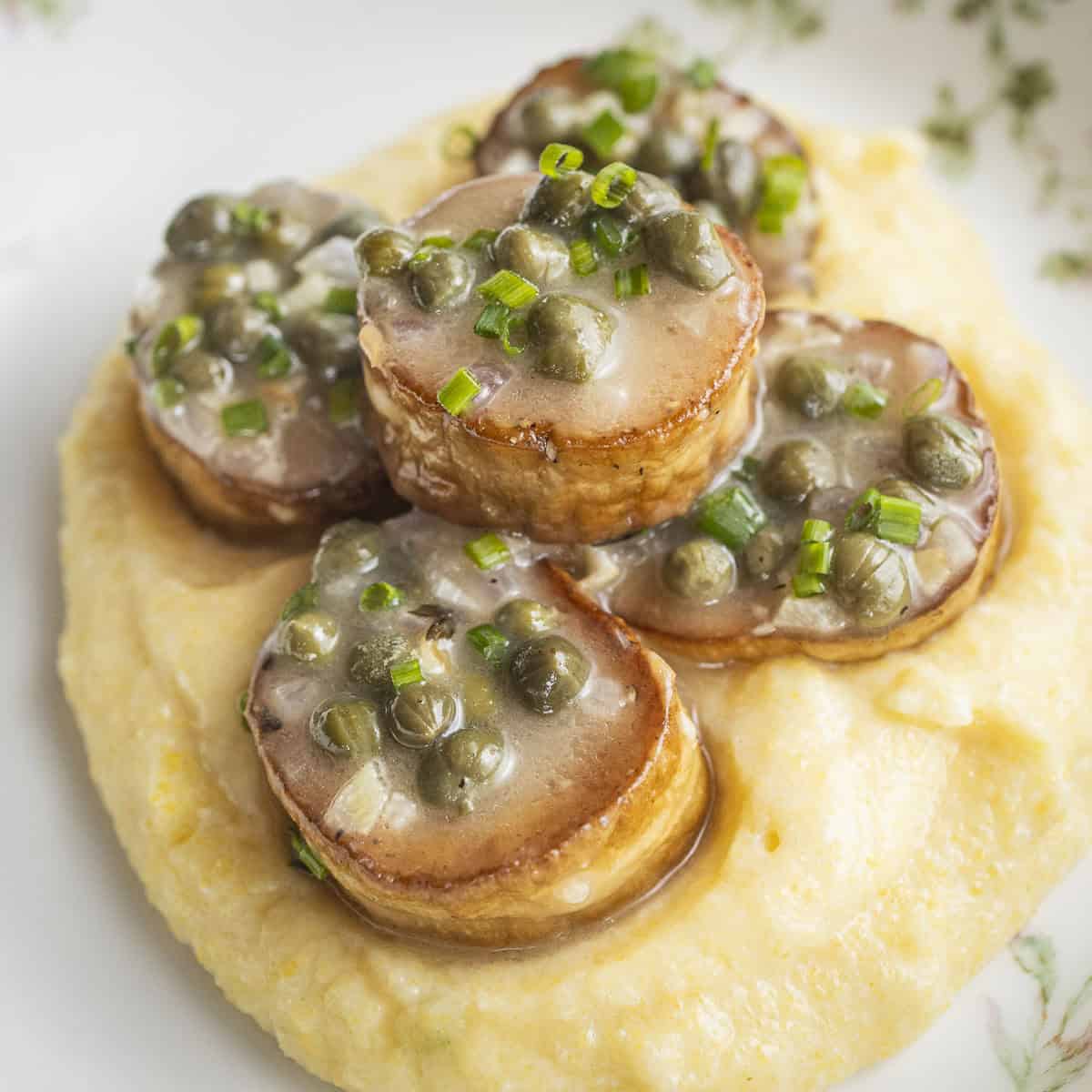 Golden-brown king oyster mushroom scallops plated with polenta, capers, lemon, and herbs.