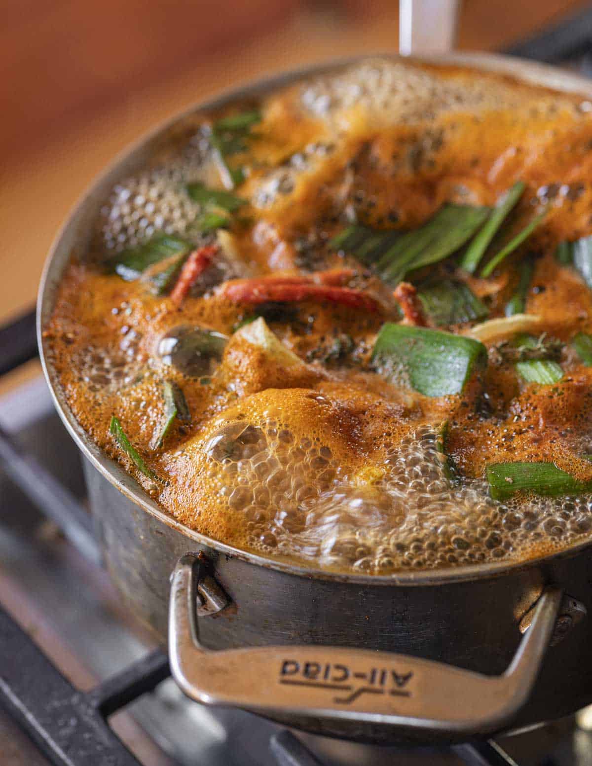 Bringing a pot of lobster shells, water, vegetables and herbs to a boil in a pot.
