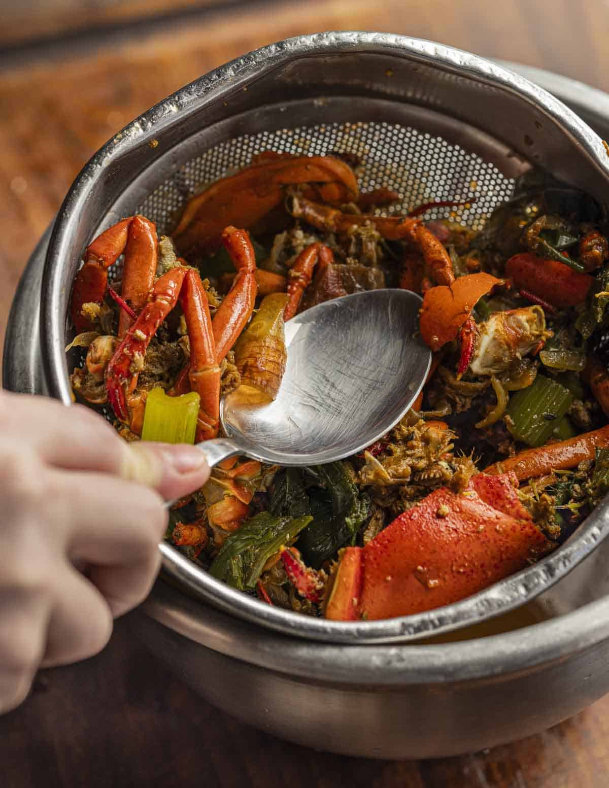 Pressing on the lobster shells to remove as much of the stock as possible.