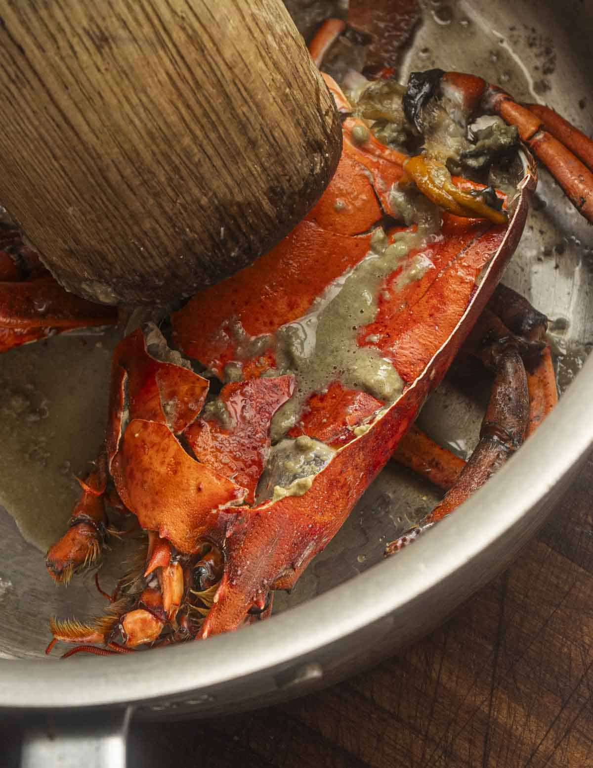 A close up image of crushing lobster heads with a mallet showing the tomalley coming out.