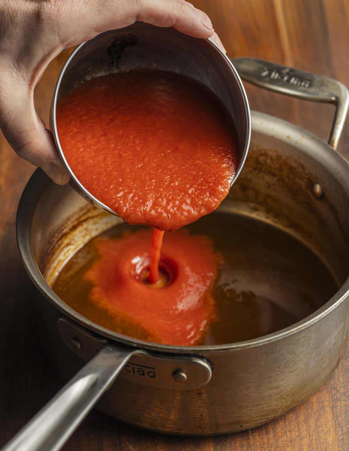 Adding seedless tomato purée to a pot of reduced lobster stock.
