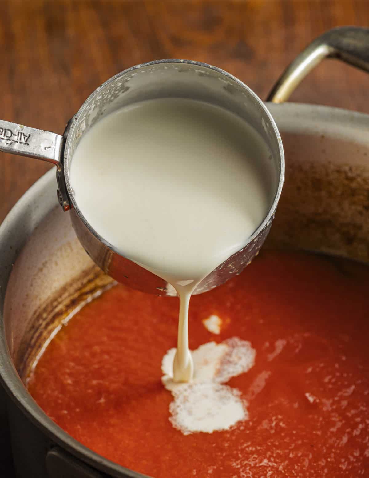 Adding heavy cream to a pot of reduced lobster stock and tomato puree.