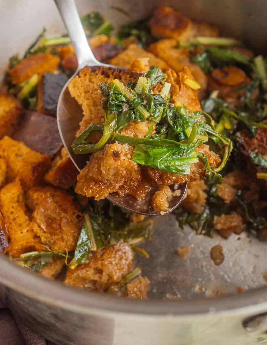A close up image of finished pane cotto showing bread and greens on a spoon with the liquid absorbed in the pan.