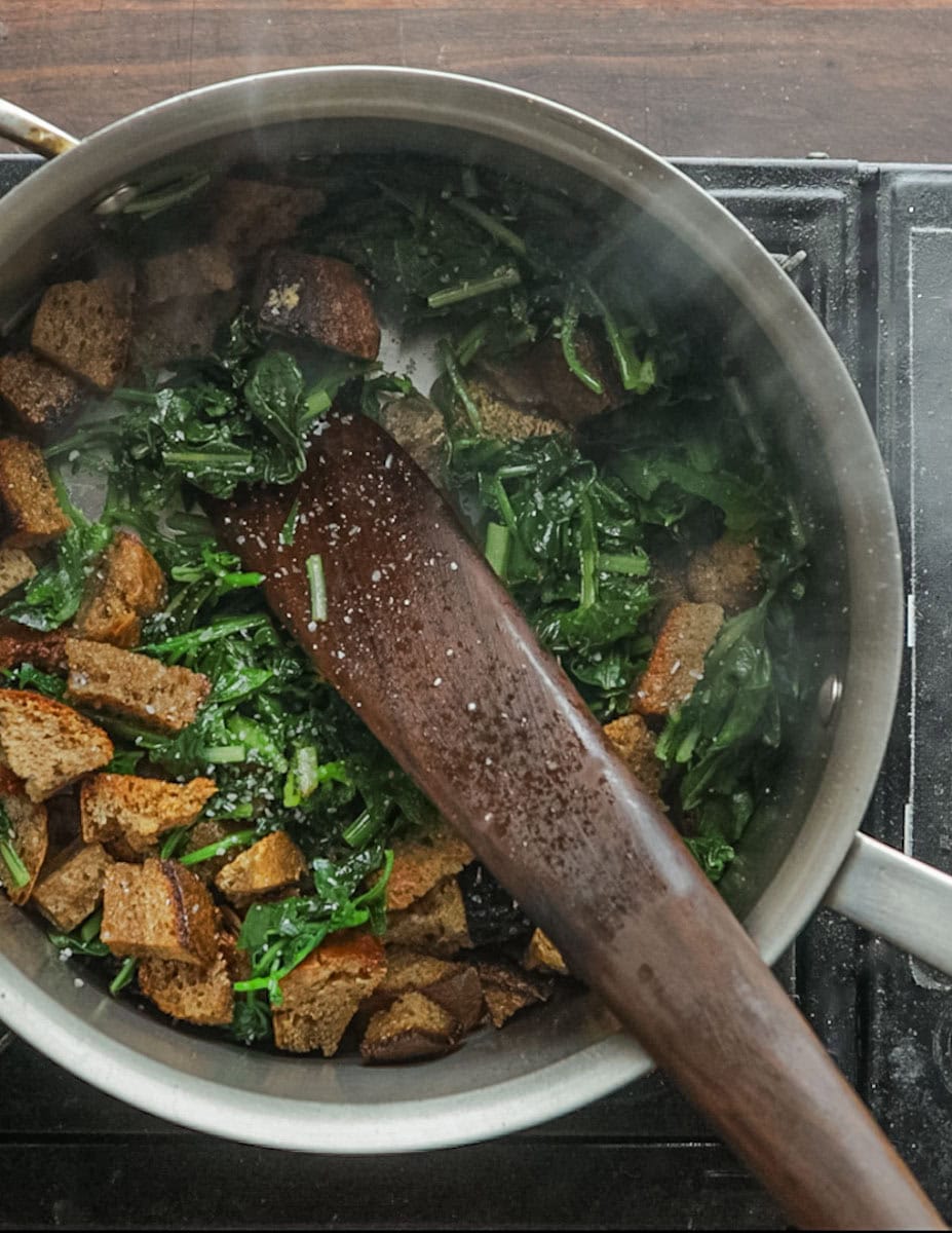 Adding greens and bread to garlic and oil in a pan to make pane cotto.