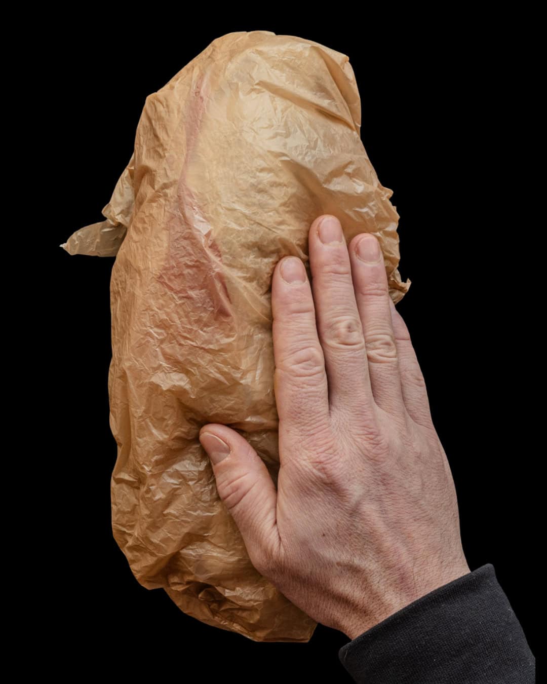 A hand wrapping a bundle of common mallow greens in a towel inside of a plastic bag for storing in the fridge.