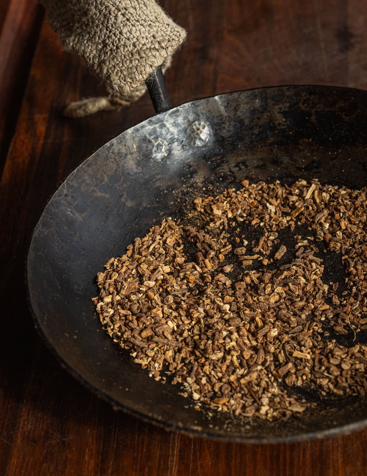 A carbon steel pan filled with darkly roasted dandelion roots.