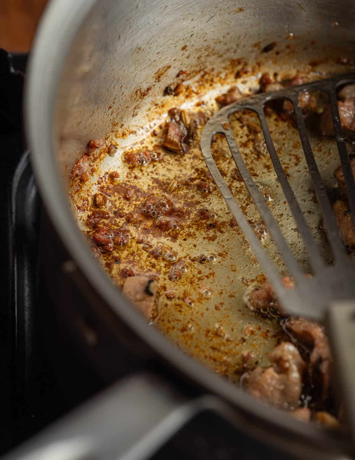 A close up image of browned bits in a pan leftover from cooking sausage.