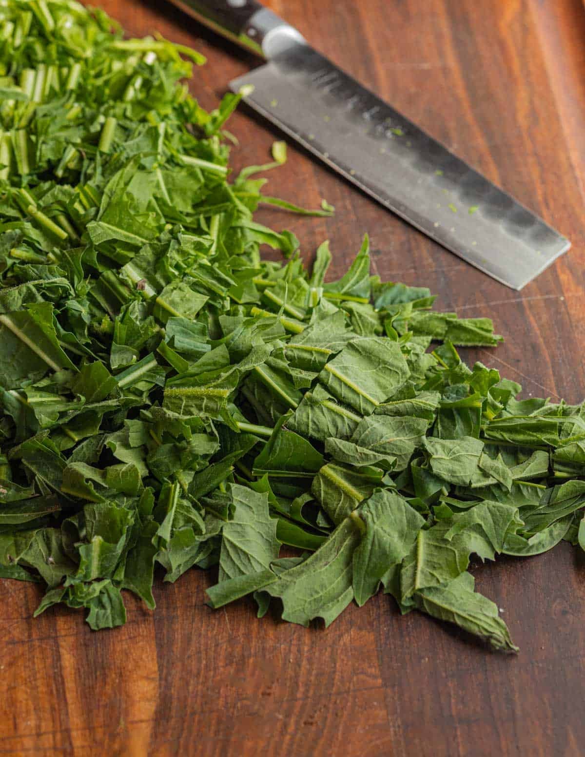 Cutting up fresh dandelion greens into bite-sized pieces on a cutting board.