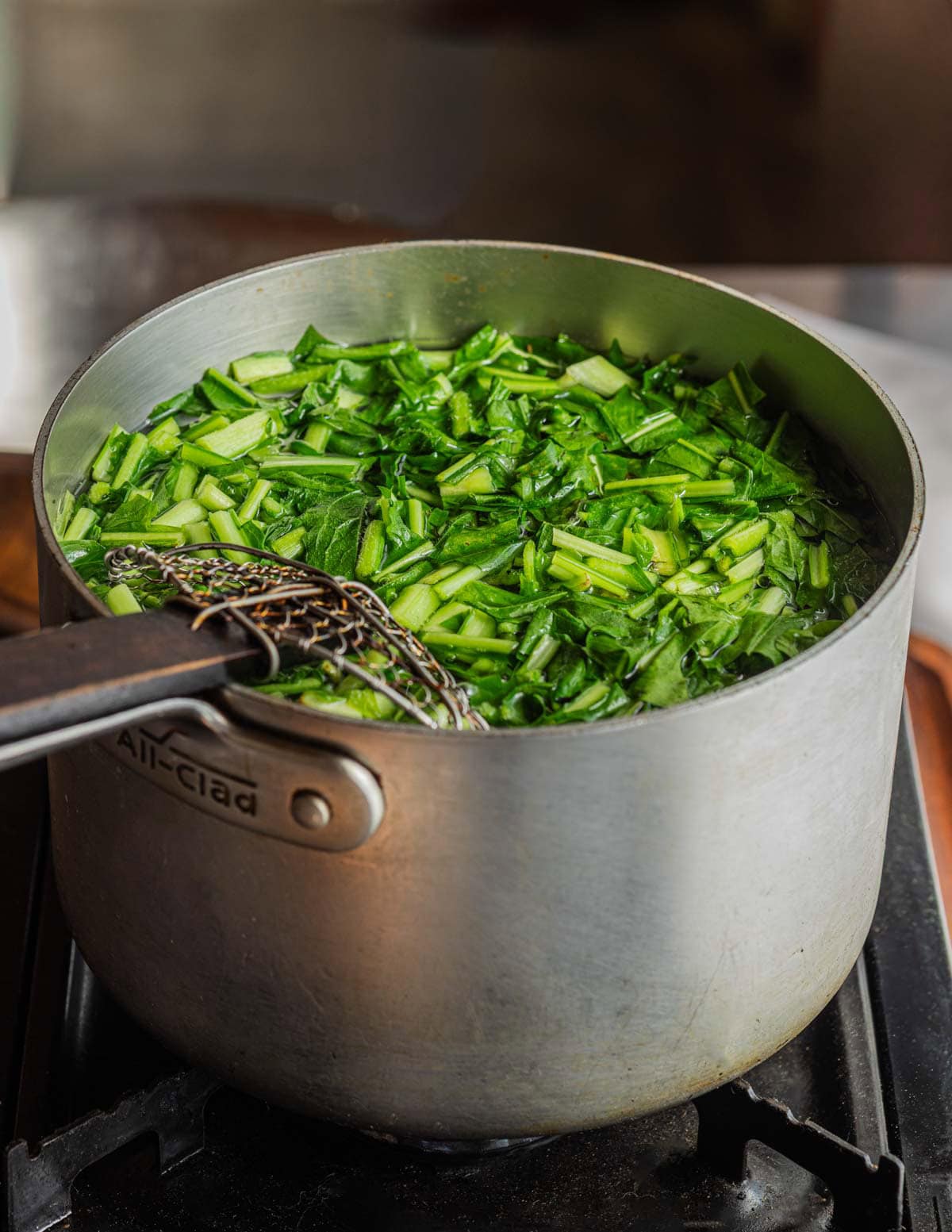 Boiling cultivated dandelion greens in a pot before adding to soup.