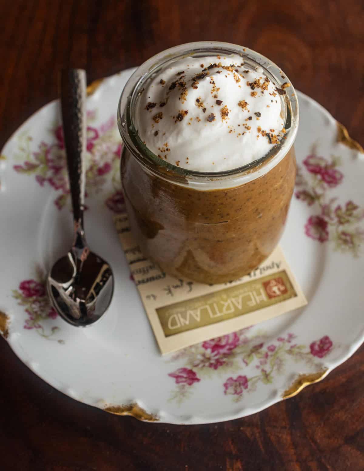 A small yogurt jar of dandelion coffee pudding with whipped cream and spicebush.