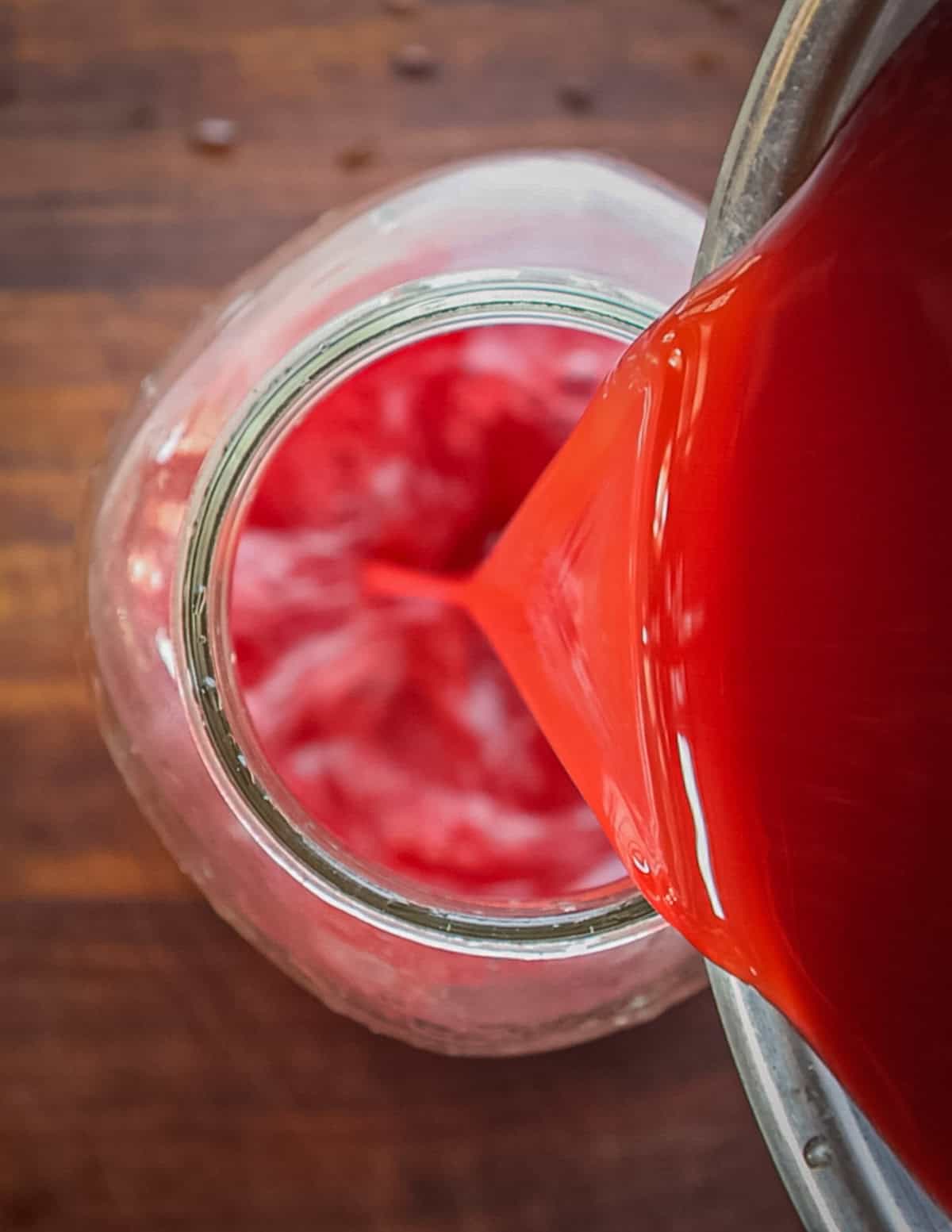 Pouring elderberry vinegar into a fresh clean jar after straining.