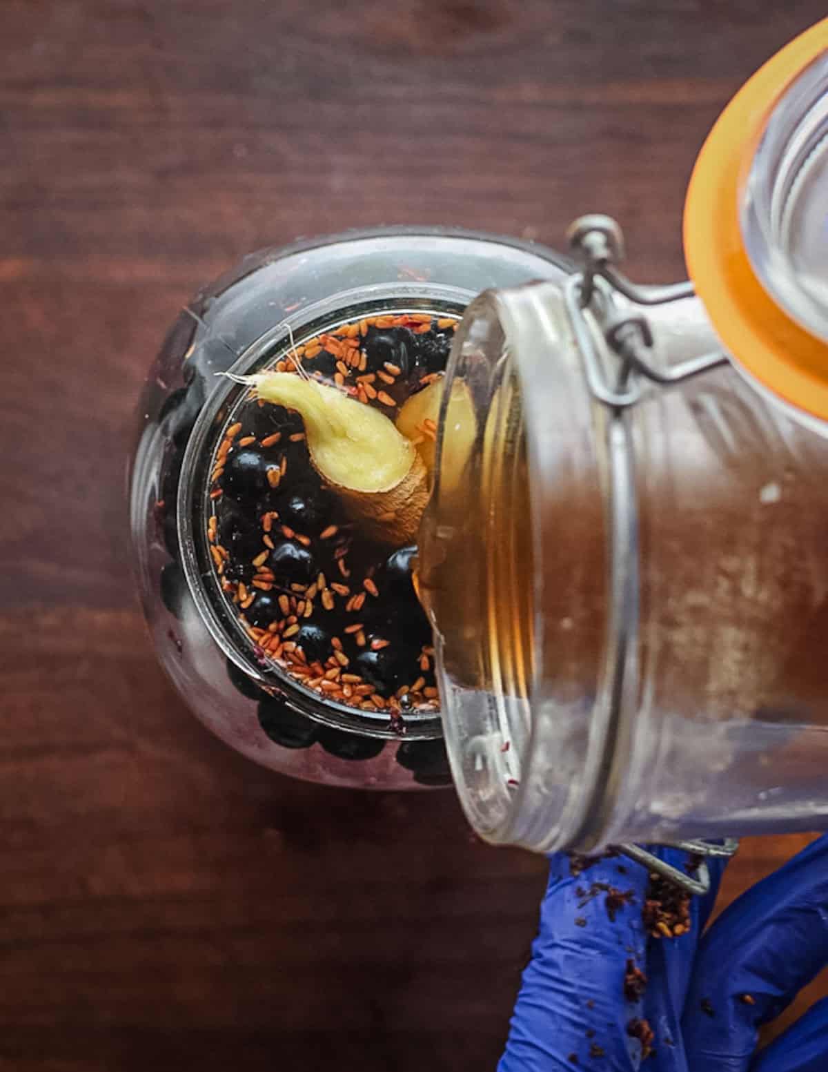 Adding living vinegar to a jar of elderberries and fruit scrap to encourage fermentation.