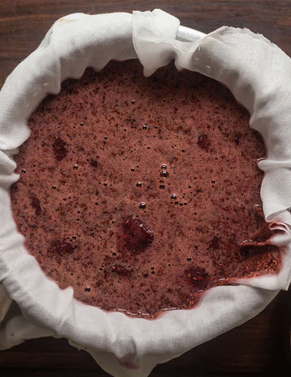 Pureed elderberries draining in a colander in cheesecloth to extract elderberry juice.