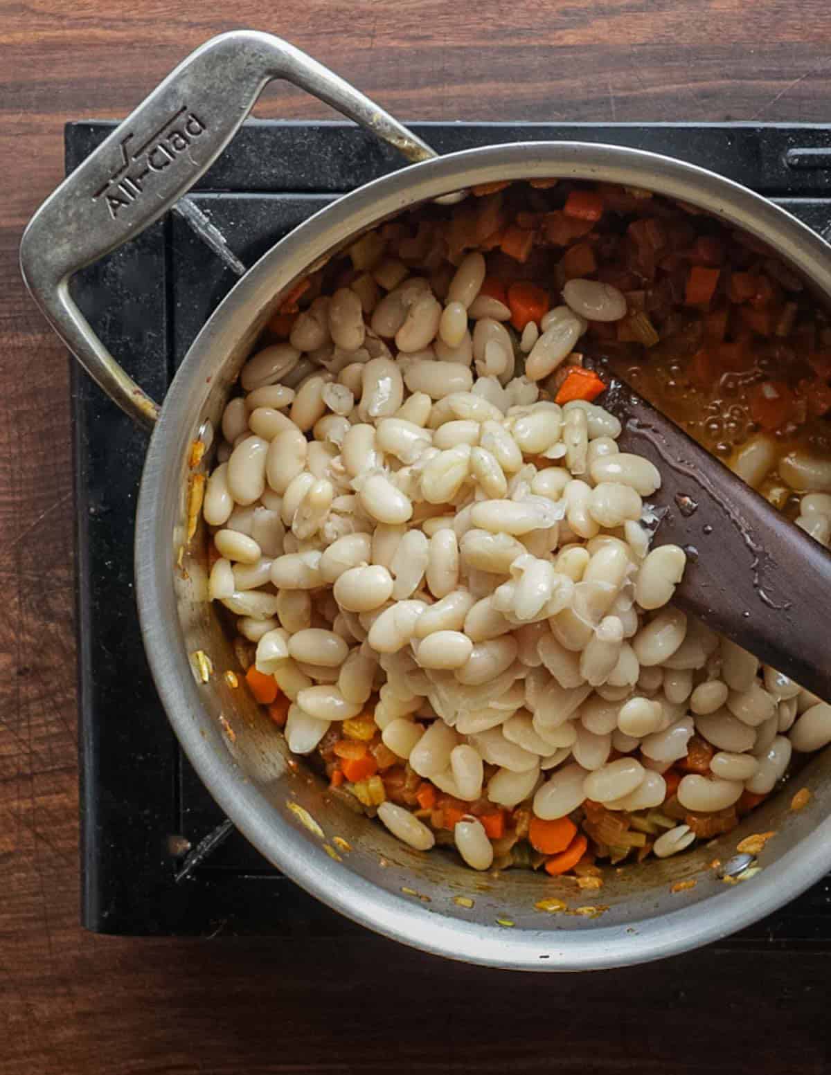 Adding cooked white beans to a pot of dandelion soup.
