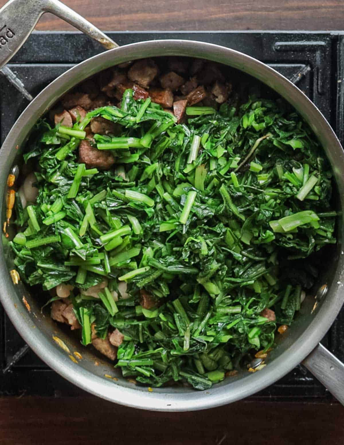 Adding blanched, sliced dandelion greens to a pot of soup before adding stock.