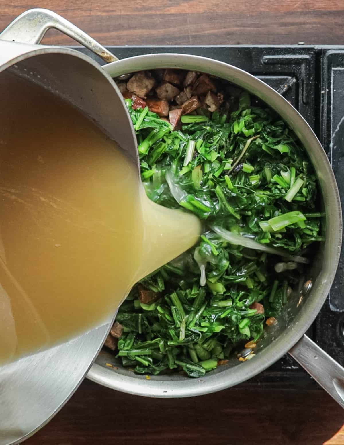 Adding chicken stock to a pot of dandelion soup.