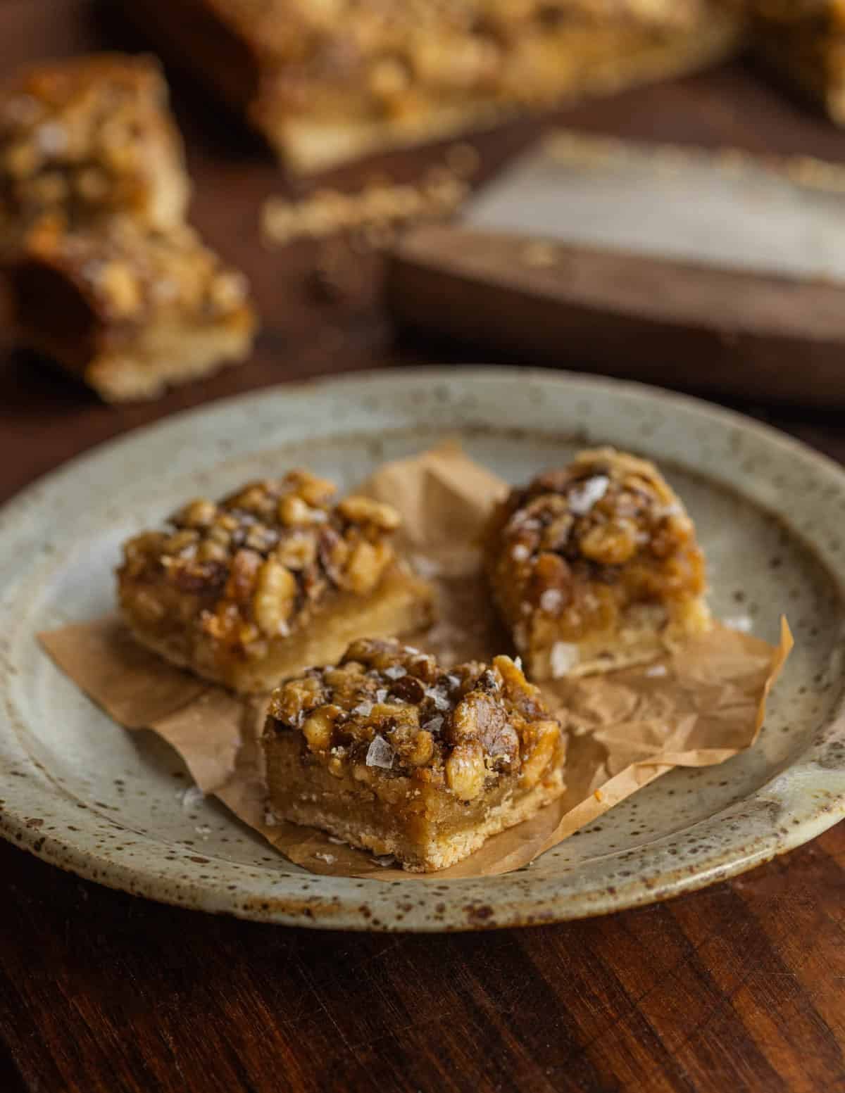 Maple walnut bars or walnut bar cookies cut and served on a plate with a bench knife and more bars in the background.