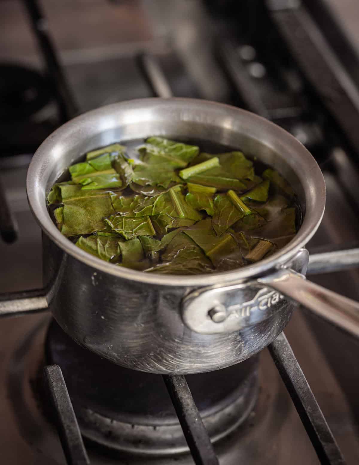 Quickly blanching dock leaves in a pot of water on the stove.