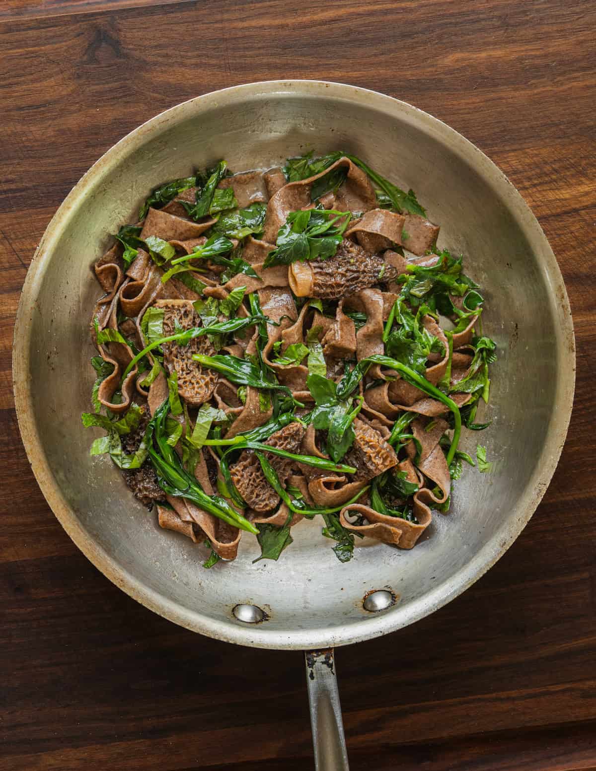 A pan of dock flour pasta tossed with morel mushrooms and spring greens.