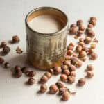 A mug of warm hazelnut milk surrounded by wild hazelnuts in the shell.