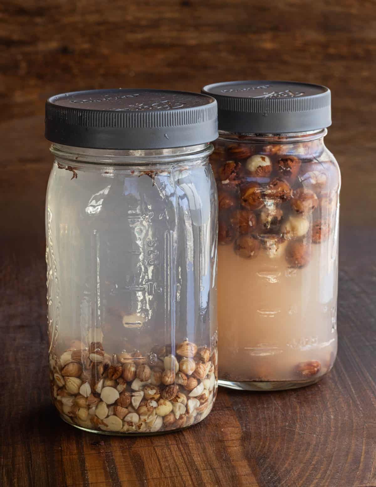 Two jars of hazelnuts soaking in water shown side by side to illustrate the opaque, tannin-rich liquid given off by the conventional hazelnuts.